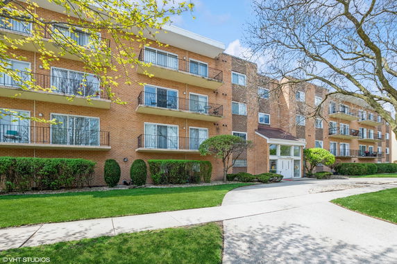 Front view of a multi-story apartment building with multiple balconies and a central entrance.