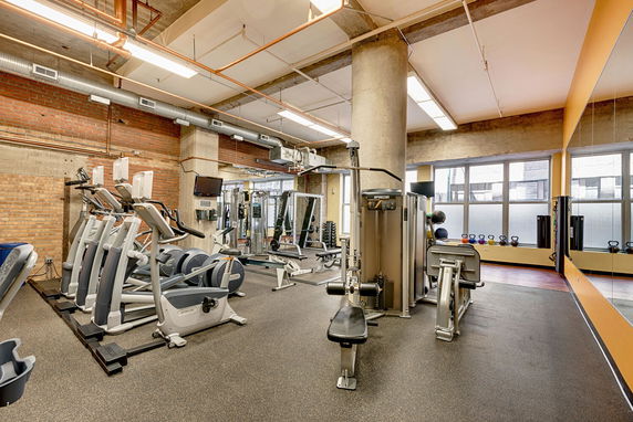 Interior view of a gym area with fitness equipment and exposed concrete pillars.