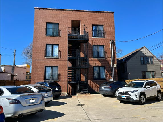 Front view of a brick apartment building with external staircases and multiple parked cars.