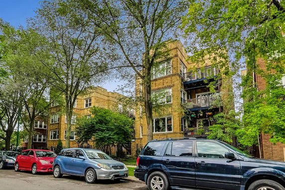 Front view of a multi-story apartment building with balconies and parked cars.