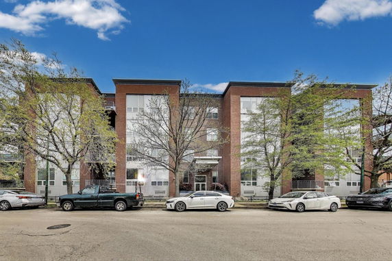 Front view of a multi-story brick building with several windows and trees in front.