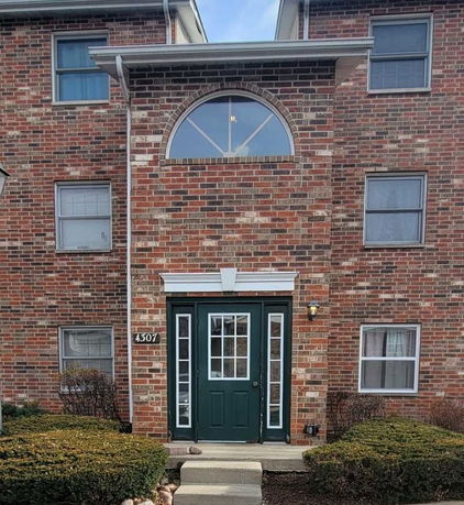 Front view of a brick multi-story building with a green door and arched window.