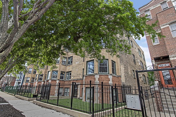 Front view of a multi-story apartment building with a brick exterior and fenced yard.