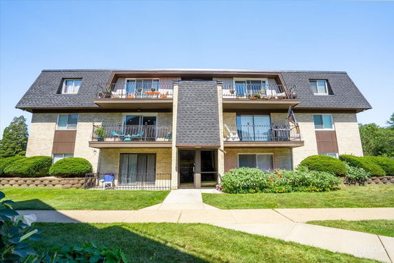 Front view of a three-story apartment building with balconies and sloped roof.