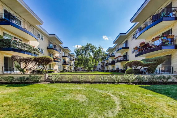 Front view of multi-story apartment buildings with balconies surrounded by landscaped greenery.
