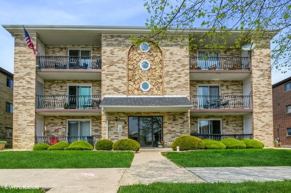 Front view of a three-story brick apartment building with balconies and a central entrance.
