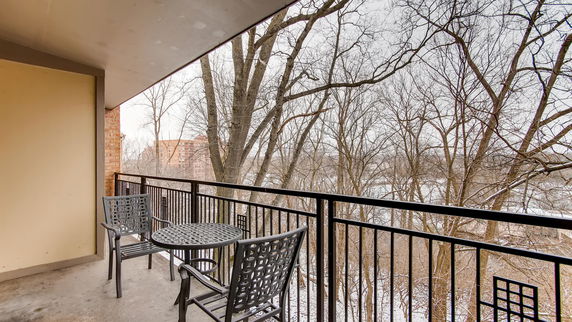 Balcony with metal table and chairs overlooking trees and distant buildings.