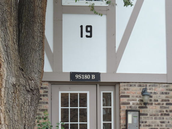 Front view of a building with a white and brick facade, featuring a prominent number '19' and a door with a keypad entry system.