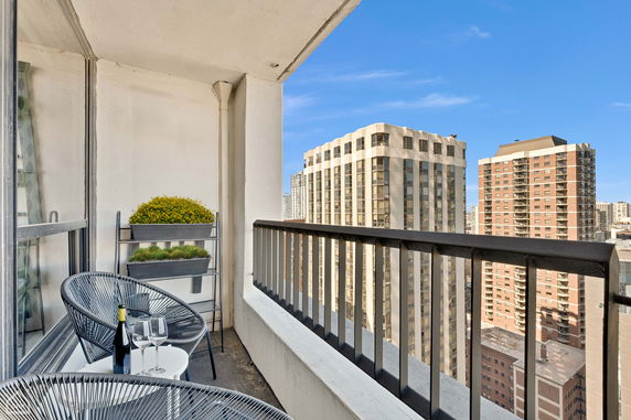 Balcony with chairs and plants, overlooking city buildings.