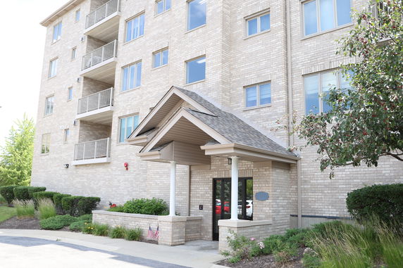Front view of a multi-story brick apartment building with balconies and a covered entrance.
