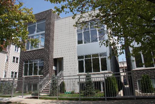 Front view of a modern two-story house with large windows and a metal fence.