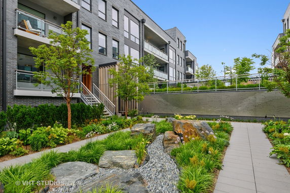 Front view of a modern multi-story apartment building with balconies and a landscaped garden.