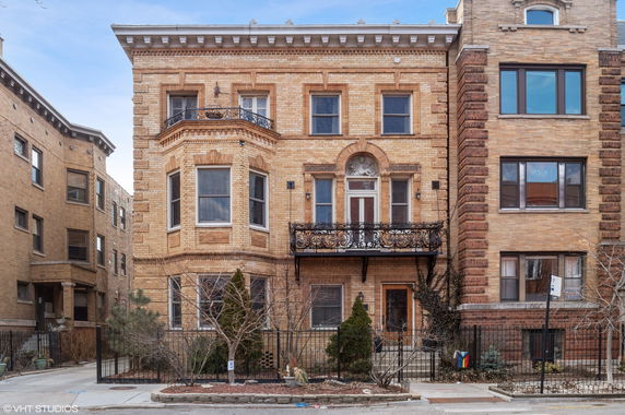 Front view of a multi-story brick building with ornate balcony and arched windows.