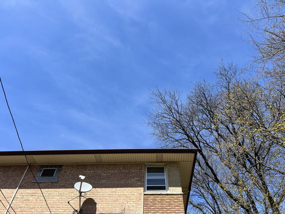 Partial view of the upper section of a brick building with a satellite dish and windows.