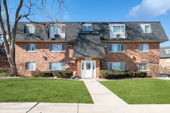 Front view of a brick apartment building with multiple windows and a shingled roof.