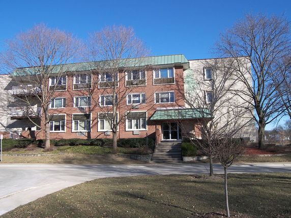 Front view of a multi-story brick building with a green roof and multiple windows.