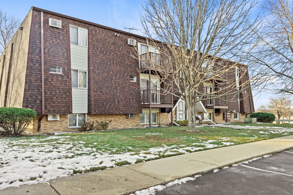 Front view of a multi-story apartment building with balconies and brown shingles.