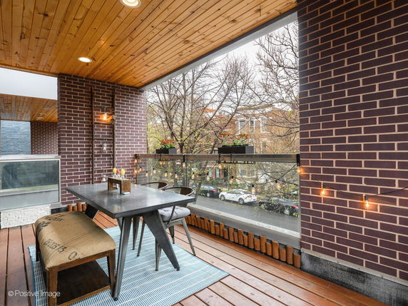 Covered balcony area with brick walls, seating arrangement, and view of trees and street.