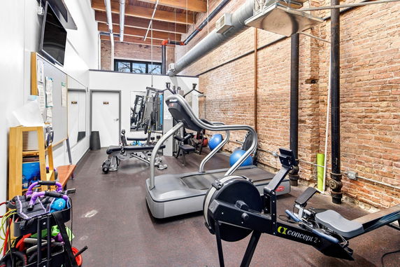 Indoor gym with exercise equipment against a brick wall.