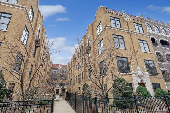 Front view of a multi-story brick apartment building with ornate door and many windows.
