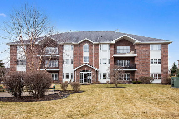 Front view of a three-story brick apartment building with multiple balconies and large windows.