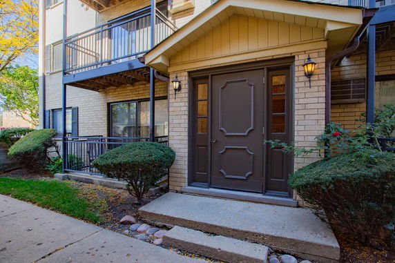 Front view of a building entrance with a porch and small bushes.