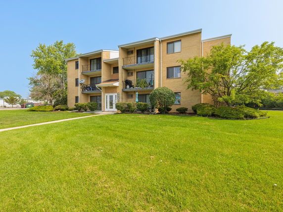 Front view of a three-story brick apartment building with balconies.