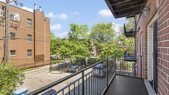 View from a balcony of a brick apartment building overlooking neighboring buildings and trees.