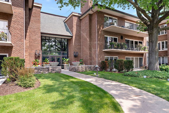 Front view of a brick multi-story building with balconies and a landscaped entrance.