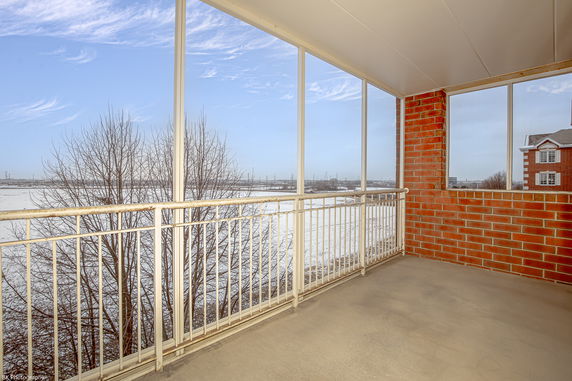 Enclosed balcony with red brick walls and metal railings overlooking a snowy landscape.