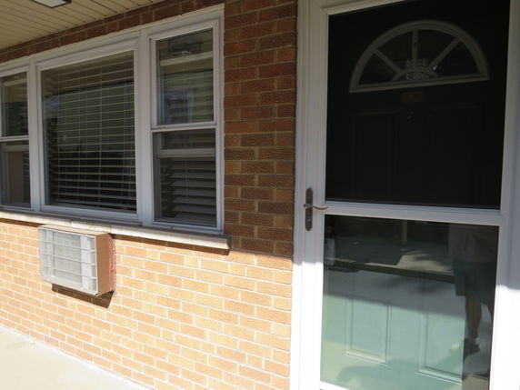 Front view of a house with a brick exterior, a window with blinds, and a door with an upper window panel.