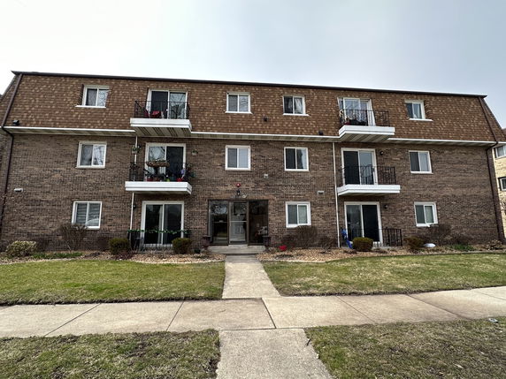 Front view of a three-story brick apartment building with balconies.