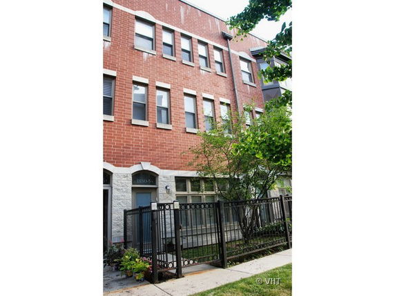 Front view of a multi-story brick townhouse with a fenced entrance.
