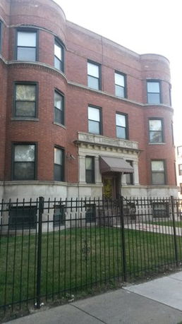 Front view of a three-story brick building with arched windows and a fenced yard.