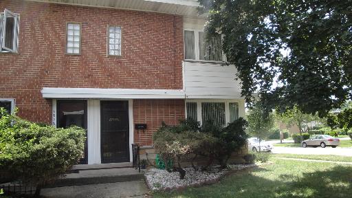 Front view of a two-story brick house with shrubs and trees.