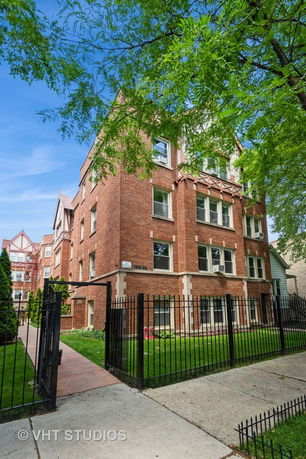 Front view of a multi-story brick apartment building with metal fencing.