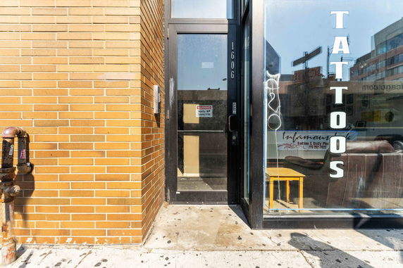 Front view of a tattoo shop entrance with glass door and brick wall.