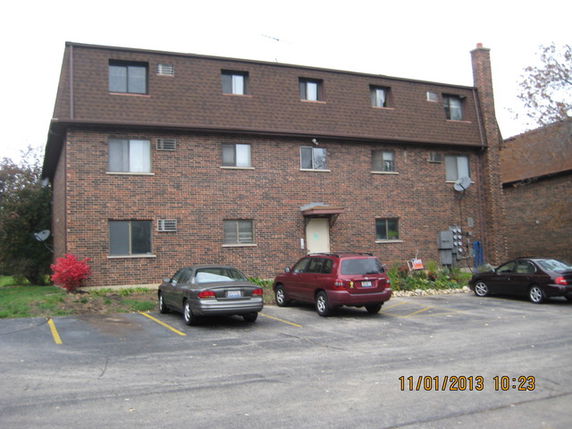 Front view of a three-story brick apartment building with a parking area in front.