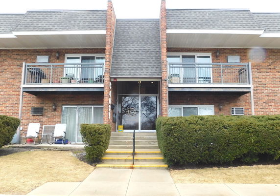 Front view of a two-story brick apartment building with balconies and a central entrance.