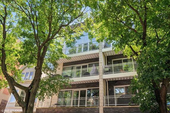 Front view of a multi-story residential building with balconies and trees.