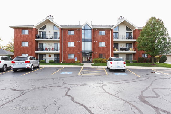 Front view of a three-story brick apartment building with balconies.