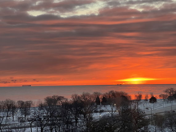 Panoramic view of a sunset over a snowy landscape with a body of water and ship.