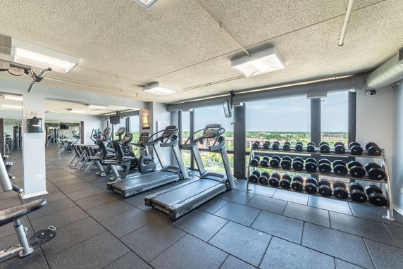 Indoor gym with exercise equipment and a view through large windows.