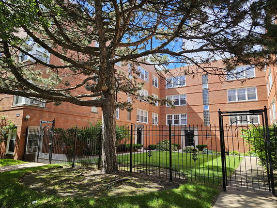 Front view of a multi-story brick apartment building with a gated entrance.