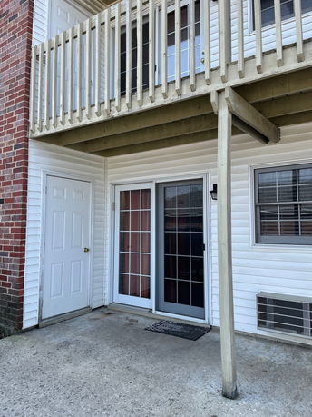 View of the lower level exterior of a two-story building with sliding glass doors and a balcony.