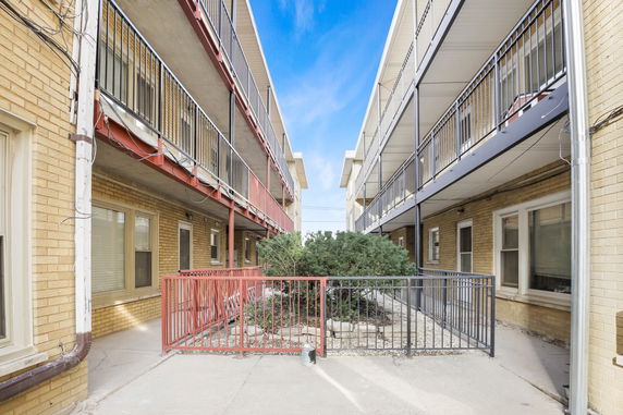 View between two apartment buildings with metal railings and a small shrub area in the center.