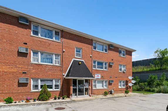 Front view of a three-story brick apartment building with multiple windows and air conditioning units.