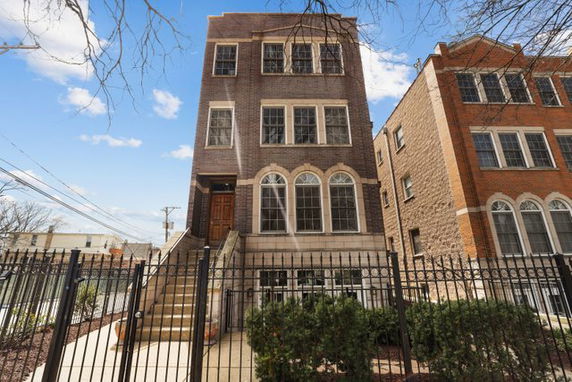 Front view of a multi-story brick apartment building with fenced entrance.