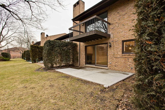 Back view of a two-story brick house with a small balcony and sliding glass door.