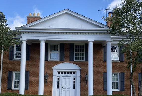 Front view of a two-story brick building with white columns and a triangular pediment.
